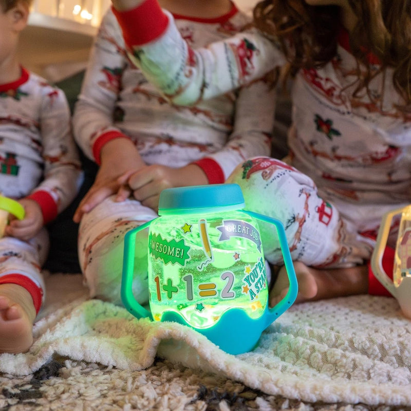 Blue Glo Pals sensory jar glowing green beside children in festive pyjamas, decorated with number and reward stickers