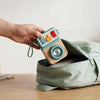 Hand placing the compact Busy Camera activity toy into an open backpack
