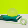 Speks Gump Jumbo Algae stress ball resting on stacked teal notebooks
