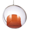 A modern hanging glass egg chair with a clear transparent spherical dome, a silver metal rim, and an orange upholstered seat, suspended by a chain against a white background.