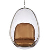 A modern egg-shaped hanging pod chair with a clear transparent shell and a brown satin cushioned seat and backrest, suspended by a metal chain against a white background.