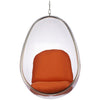 A modern egg-shaped hanging chair with a clear transparent shell and an orange upholstered seat and back cushion, suspended by a metal chain against a white background.