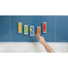 Hand playing Melody Chimes with a yellow mallet, with five bars attached to blue tiles above a bath.