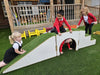 Children playing on a white outdoor climbing structure with green turf surfaces in a schoolyard setting.