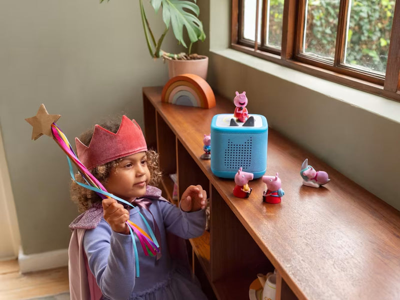 Child beside a blue Toniebox and several Peppa Pig Tonies, available separately