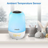 A Vtech ambient temperature sensor alarm clock with a blue and white body, shown on a shelf next to small stuffed toys with a blurred window background. Blue text at the top reads 'Ambient Temperature Sensor'.